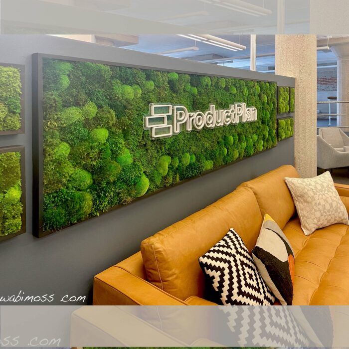Moss artwork above an orange couch. The moss has a company logo in the middle.